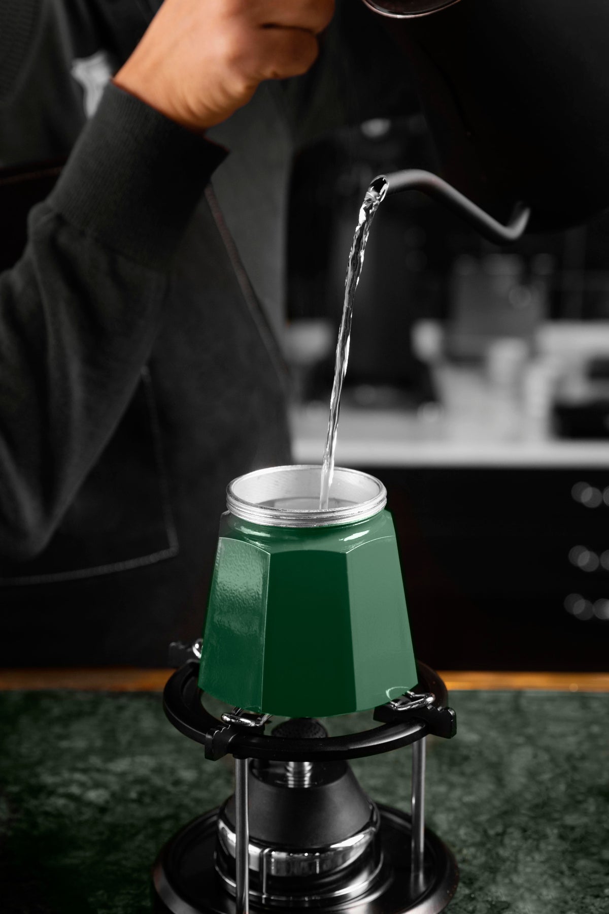 Un barista versant de l'eau chaude avec une bouilloire dans la base d'une cafetière à l'italienne.