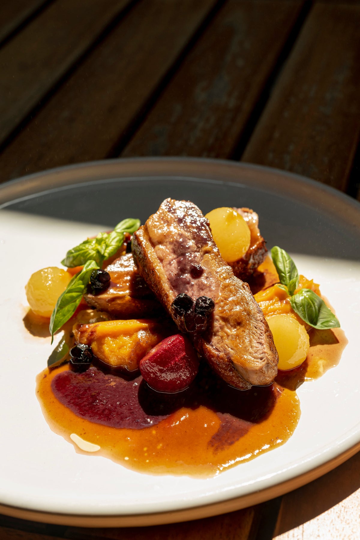 assiette blanche dressée avec un magret de canard infusé au café, ses légumes et quelques olives et brins de basilic