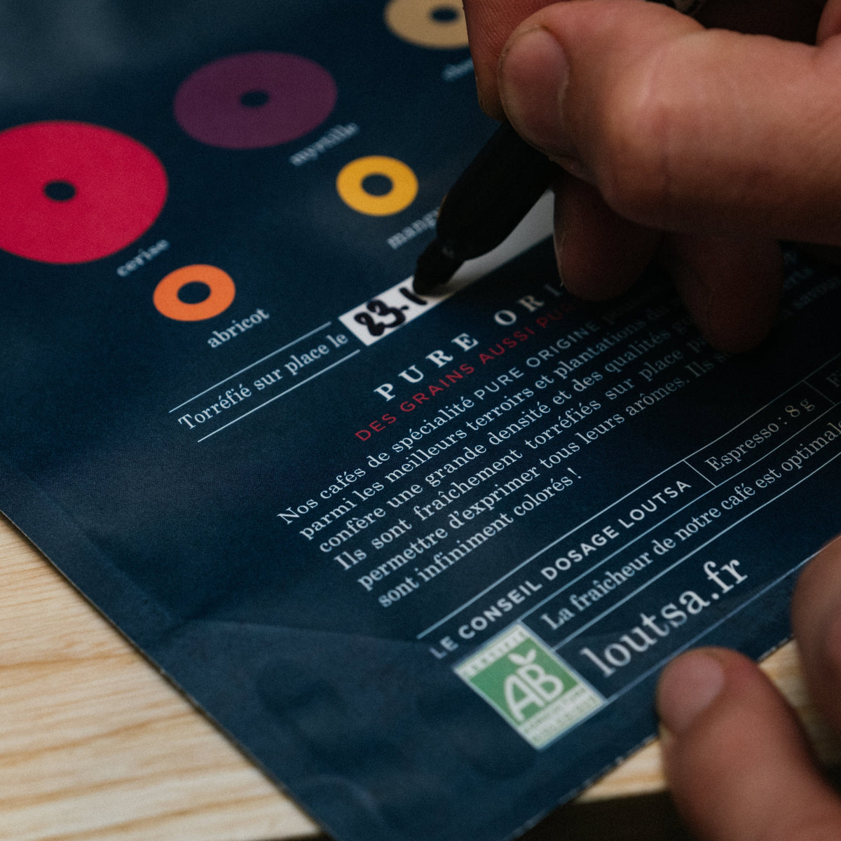 sachet de café vide sur lequel une main écrit la date de torréfaction au marqueur noir
